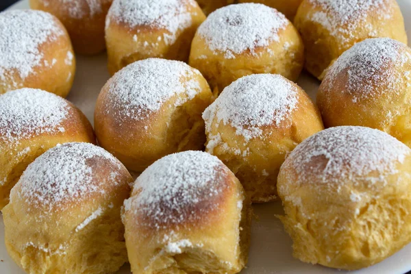 Round buns with white powdered sugar on a white plate side view.
