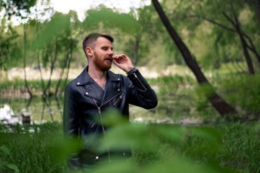 Kızıl bıyıklı ve sakallı bir adam yeşil bir ormanda sağa bakarken bıyığıyla titriyor..