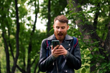 Yoğun bir ormanda dikilirken akıllı telefondan mesaj okuyan kalın sakallı bir adam şaşkınlıkla ağzını açtı..
