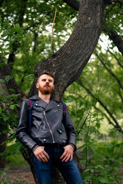 Genç bir adam ağaca yaslanıyor ve yukarı bakıyor..