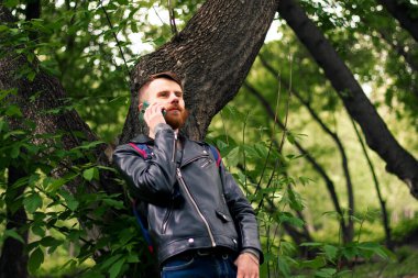 Sakallı adam ormanda telefonla konuşuyor..