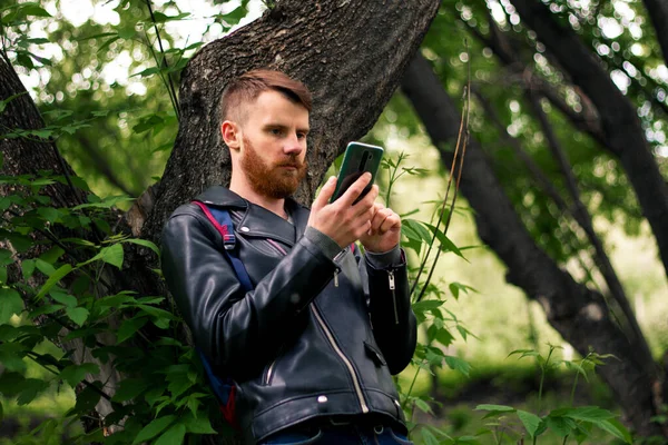 Bir ağaç dalına uzanıp yeşil bir ormanın ortasındaki akıllı telefon ekranına bakar..