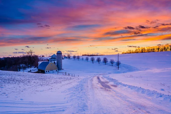 Puesta de sol sobre una carretera cubierta de nieve y una granja en una zona rural de Yo —  Fotos de Stock