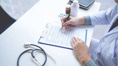 Doktor bir belge raporunu okuyor ve evrak işleriyle ilgili yazı yazıyor.