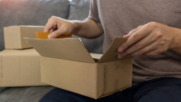 Startup small business entrepreneur SME, young asian man working with laptop computer and delivery packaging box, online market packing, SME e-commerce seller concep