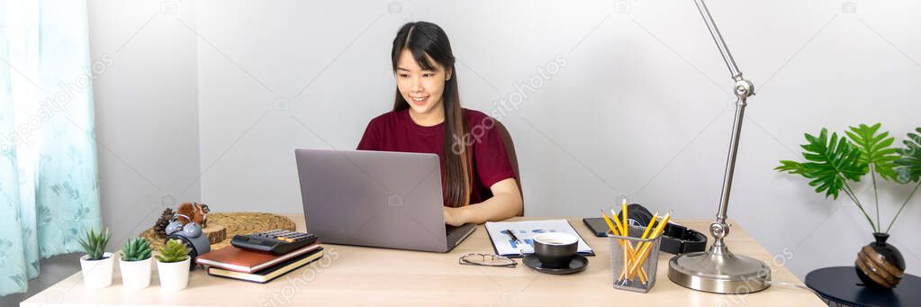 A young, beautiful relaxing business asian girl use a laptop working remotely from home on desk as a freelancer, quarantine for Coronavirus and smart working concept