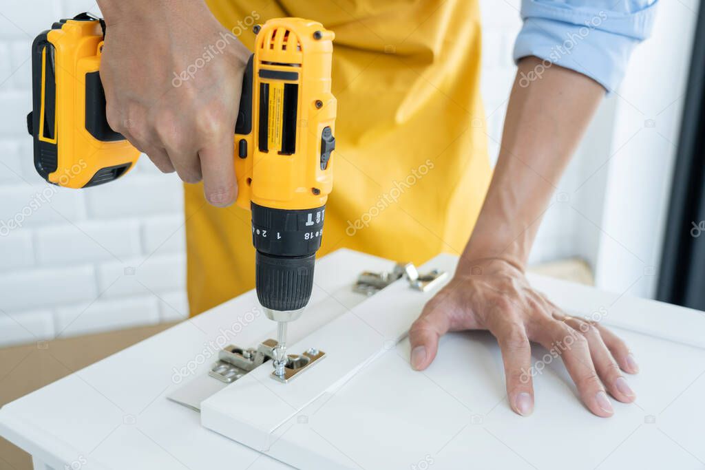 close up man holding cordless screwdriver machine and screws lie for screwing a screw assembling furniture at home