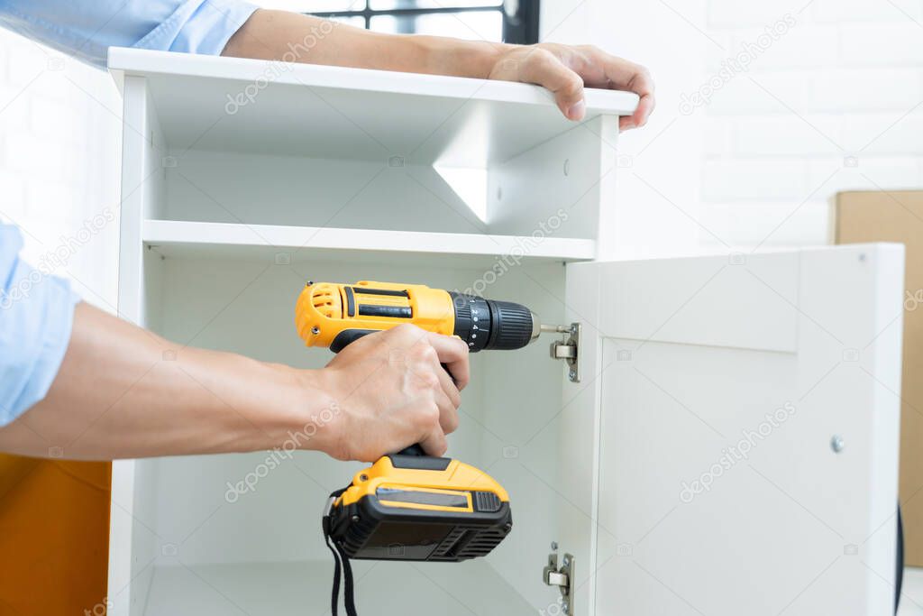 close up man holding cordless screwdriver machine and screws lie for screwing a screw assembling furniture at home