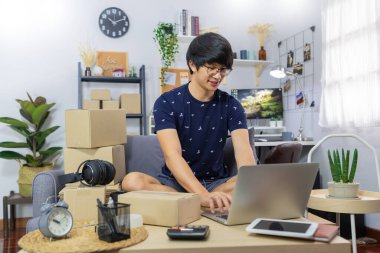 Evinde çalışan genç Asyalı erkek iş sahibi Business Online için başla kontrol etmek için dizüstü bilgisayarla çalış, müşteriye sipariş vermek için çevrimiçi paket teslimatı yap, e-ticaret konsepti