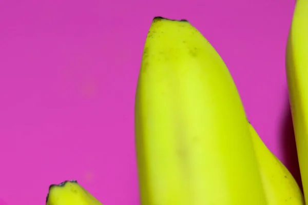 Bright yellow banana close-up on a bright pink or purple background top view. Copy space