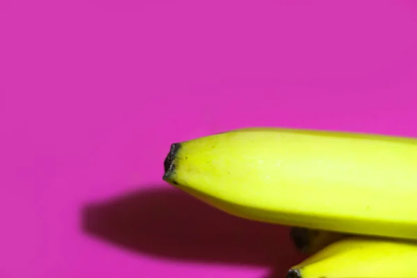 Jasnożółty banan zbliżenie na jasnoróżowym lub fioletowym tle widok z góry. Przestrzeń kopiowania — Zdjęcie stockowe