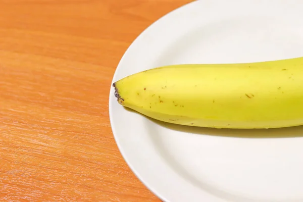 Plátano en un plato blanco sobre una mesa de madera con espacio para copiar a la izquierda. Nutrición saludable para mantener la salud — Foto de Stock