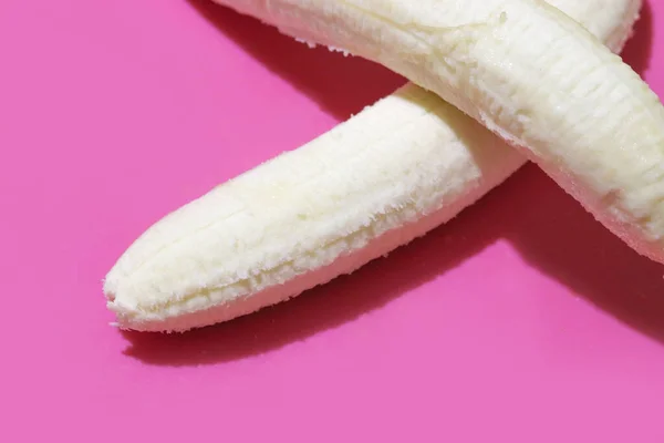 Obierany banan leży na innym na różowym lub fioletowym tle. Kopiuj miejsce na tekst — Zdjęcie stockowe