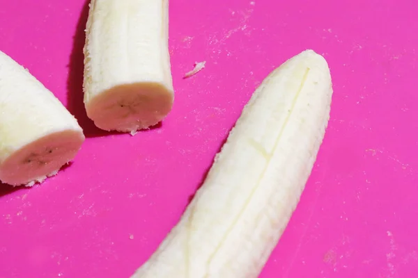 Banan w plasterkach na różowym biurku. Zbliżenie na fioletowe tło z miejsca kopiowania — Zdjęcie stockowe