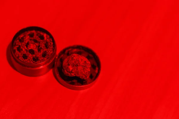 Κοντινό πλάνο φαρμακευτική μαριχουάνα σε μύλο σε ένα τραπέζι με κόκκινο φωτισμό. Χρήση ναρκωτικών για ιατρικούς σκοπούς. Αντιγραφή χώρου — Φωτογραφία Αρχείου