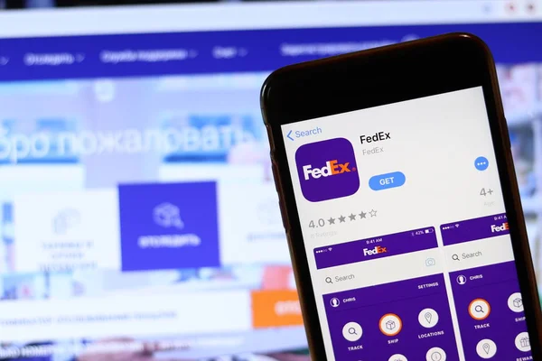 Телефон с иконкой FedEx на экране крупным планом с размытием сайта на ноутбуке. Лос-Анджелес, штат Калифорния, США - 30 ноября 2019 года — стоковое фото