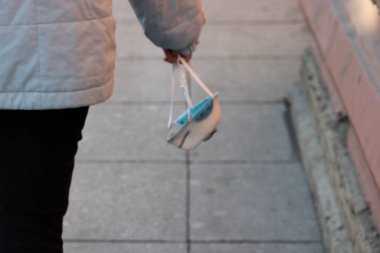 Bir kadın elinde bir solunum cihazı tutuyor ve cadde boyunca yürüyor. Virüslere, enfeksiyonlara ve bakterilere karşı tıbbi koruyucu maske. Boşluğu kopyala.