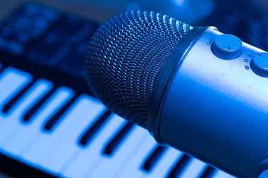 Müzik üretim konseptini izler. Mavi ışıkta arkaplanda mikrofon ve sentetik klavyeli stüdyo.