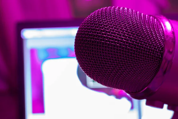 Pro microphone for broadcast with laptop on background in purple light. Podcast studio with copy space.
