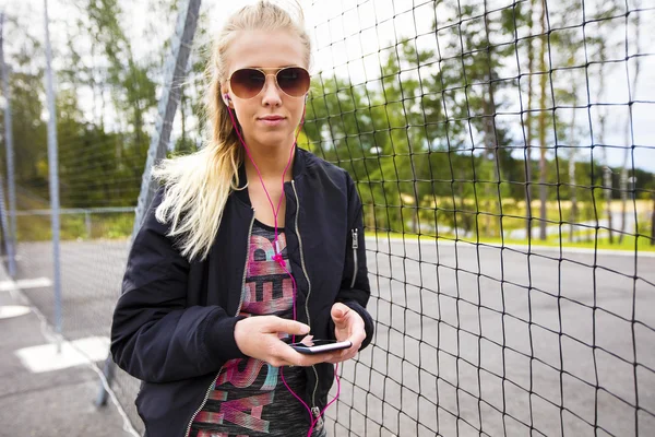 Спортивная женщина держит мобильный телефон, слушая музыку по ограде — стоковое фото