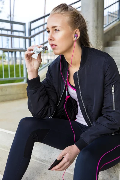 Deportiva mujer comiendo proteína bar mientras escucha música en pasos —  Fotos de Stock