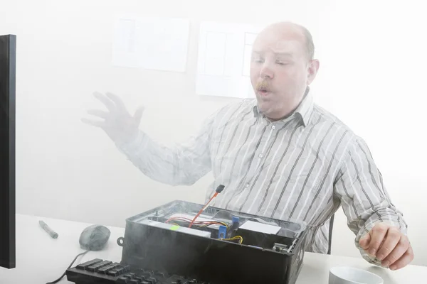 Reifer Geschäftsmann pustet im Büro Rauch aus Computergehäusen — Stockbild Geschäftsmann pustet Rauch aus Computerfahrgestell — Stockfoto