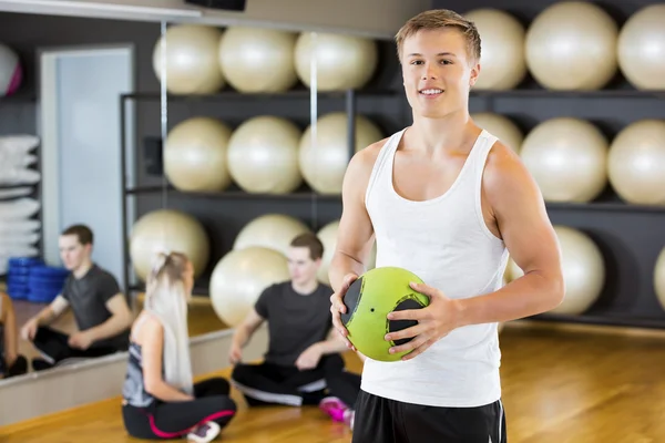 Άνδρα με αυτοπεποίθηση εκμετάλλευση ιατρική μπάλα ενώ φίλοι αναπαύεται στο γυμναστήριο — Φωτογραφία Αρχείου