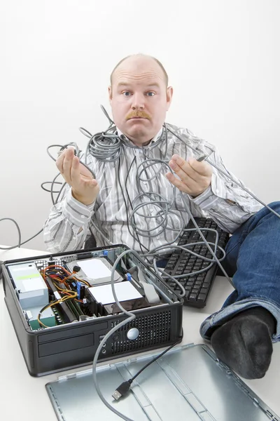 Запутавшийся бизнесмен держит запутанные компьютерные кабели за столом — стоковое фото