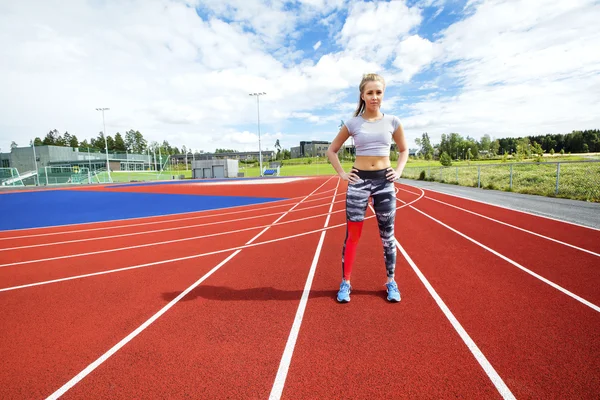 Sportig kvinna som står med händerna på höfterna på löparbanor — Stockfoto