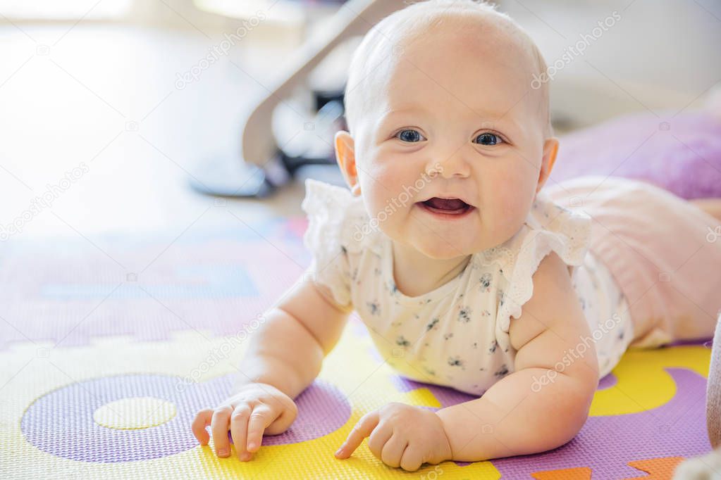 Smiling baby girl with blue eyes playing on floor mate