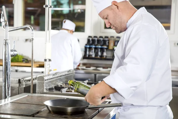 Chef derrama azeite na panela em uma cozinha profissional — Fotografia de Stock