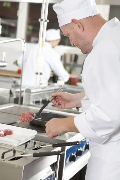 Профессиональный повар жарит говяжий стейк на кухне — стоковое фото
