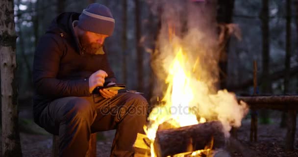 Man using compass and smart phone by campfire in the woods — Stock Video