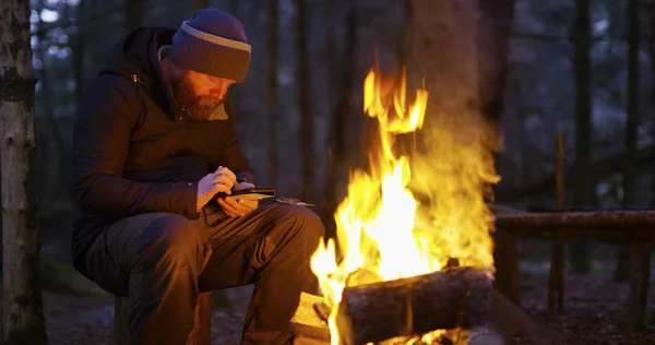 El hombre utiliza brújula y teléfono inteligente por fuego de campamento — Foto de Stock