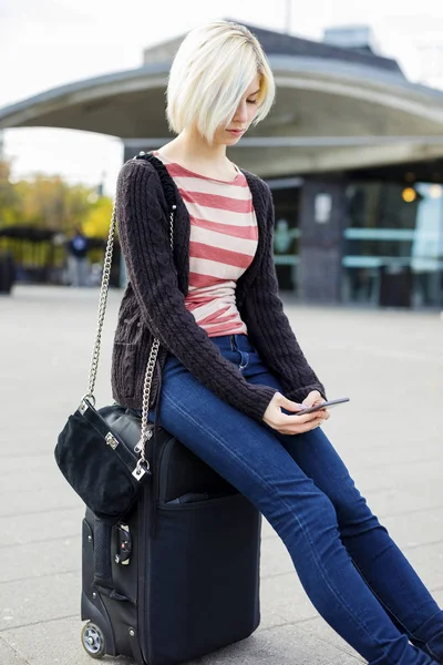 Bagaj üzerinde otururken cep telefonu kullanan genç kadın — Stok fotoğraf
