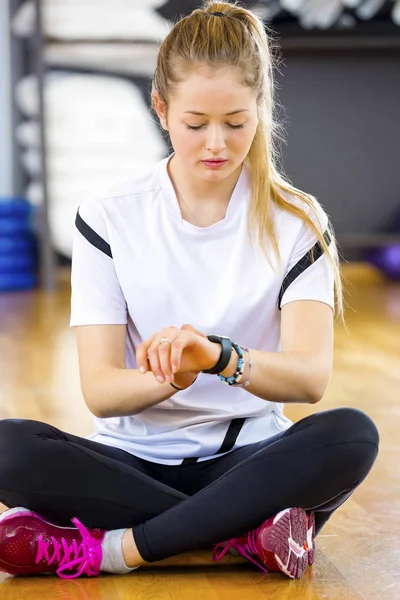 Mujer usando reloj inteligente mientras está sentado en el gimnasio —  Fotos de Stock