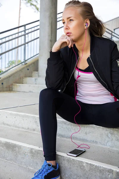Задумчивая спортивная женщина слушает музыку, сидя на ступеньках — стоковое фото