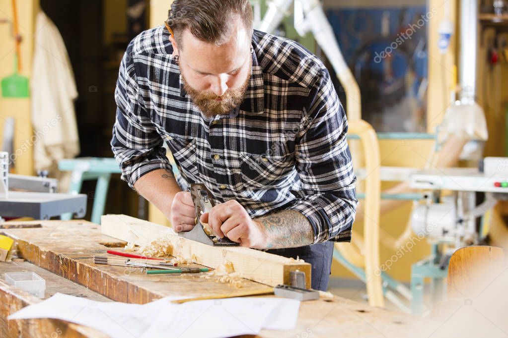 Carpenter work with plane on wood plank in workshop