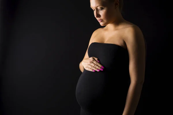 Femme enceinte réfléchie debout avec les mains au ventre — Photo