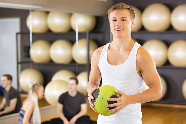 Χαμογελαστός άνθρωπος που κρατά την ιατρική μπάλα ενώ φίλοι αναπαύεται στο γυμναστήριο — Φωτογραφία Αρχείου