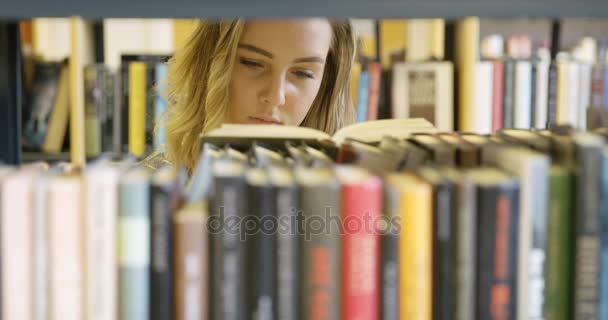 Ung kvinnlig student söker bok i skolans bibliotek — Stockvideo