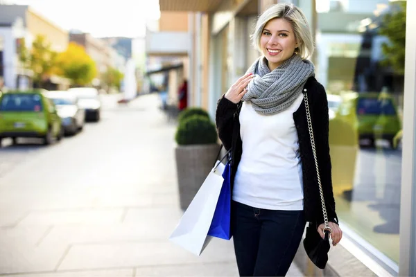 Улыбающаяся женщина с сумочкой и сумками возле магазина — стоковое фото
