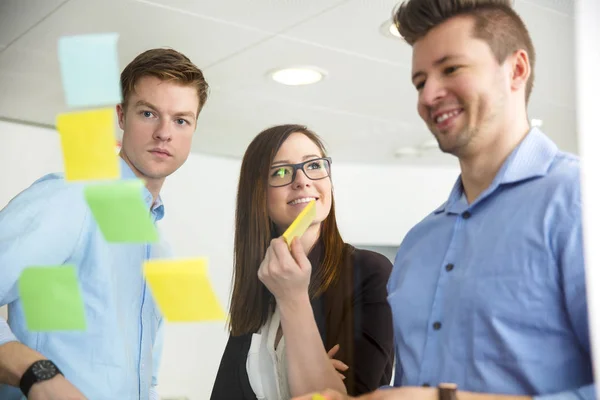 Smiling Businesswoman By Colleagues Looking At Notes Stuck On Gl — Stock Photo, Image
