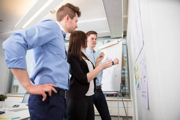 Professionals Looking At Plans Stuck On Wall In Office — Stock Photo, Image