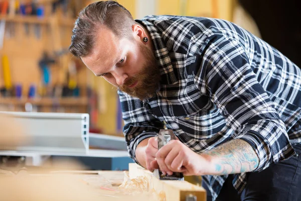 Timmerman werkt met vliegtuig op houten plank in werkplaats — Stockfoto