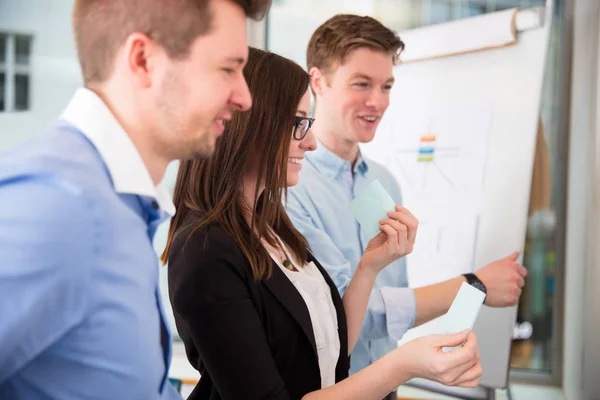 Smiling Businesswoman Holding Adhesive Note By Colleagues — Stock Photo, Image