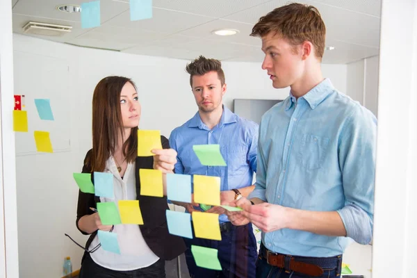 Business People Communicating While Sticking Notes On Glass — Stock Photo, Image