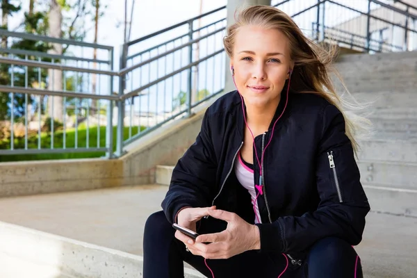 Девушка в спортивной одежде слушает музыку на мобильном телефоне — стоковое фото