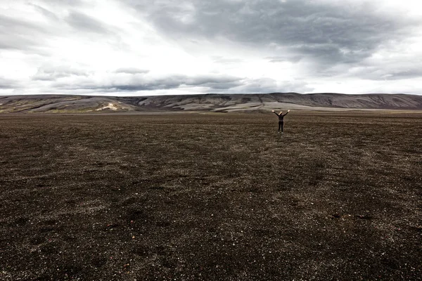 Randonneur avec les bras levés debout sur un paysage volcanique contre le ciel — Photo