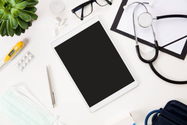Kalem ve tıbbi aletleri beyaz masa üzerinde olan tablet bilgisayar